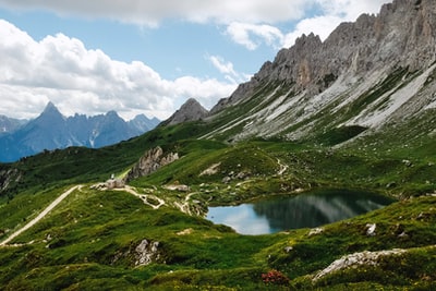 During the day, under the white clouds and blue sky, the lake is green and brown mountains
